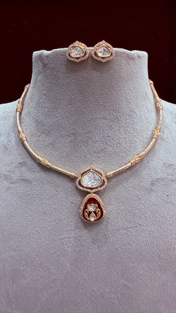 Gold-plated jewelry set featuring a necklace and matching stud earrings displayed on a light gray velvet jewelry bust. The necklace has a beaded chain with a central teardrop pendant featuring a clear heart-shaped stone and a red teardrop accent below it.