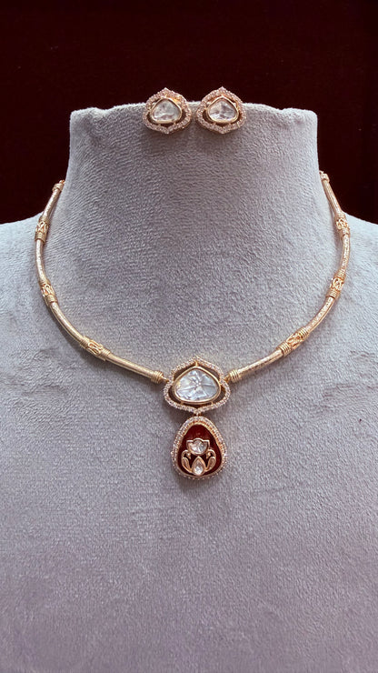 Gold-plated jewelry set featuring a necklace and matching stud earrings displayed on a light gray velvet jewelry bust. The necklace has a beaded chain with a central teardrop pendant featuring a clear heart-shaped stone and a red teardrop accent below it.