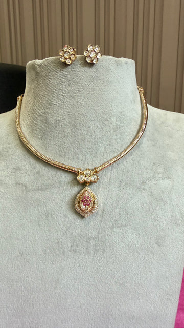 Gold-tone jewelry set on a light gray velvet mannequin bust, including a snake-style necklace with a teardrop pendant featuring a pink center and clear stones, matching flower-shaped stud earrings, and a small matching charm.
