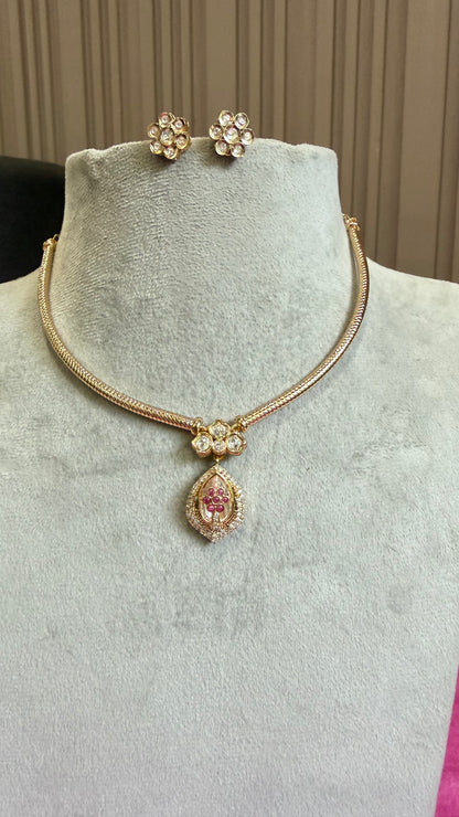 Gold-tone jewelry set on a light gray velvet mannequin bust, including a snake-style necklace with a teardrop pendant featuring a pink center and clear stones, matching flower-shaped stud earrings, and a small matching charm.