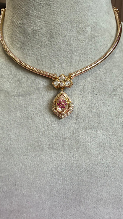 Gold-plated snake chain necklace with a teardrop pendant featuring a pink gemstone and clear stones, displayed on a gray velvet jewelry bust.