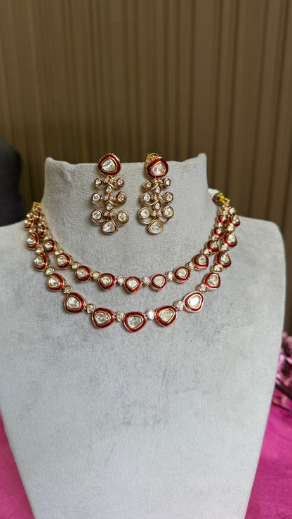 A red and gold kundan jewelry set featuring a double-strand necklace and matching drop earrings, displayed on a light gray velvet jewelry bust.