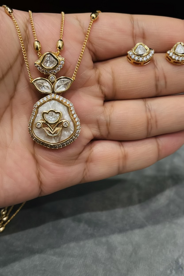 Gold-tone necklace and matching stud earrings displayed on an open hand. The jewelry features clear stones in gold settings, with a floral pendant and matching stud earrings.