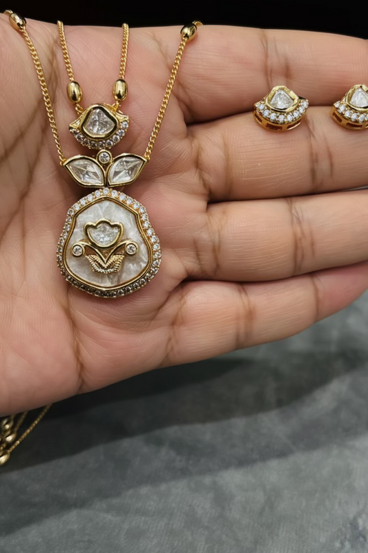 Gold-tone necklace and matching stud earrings displayed on an open hand. The jewelry features clear stones in gold settings, with a floral pendant and matching stud earrings.